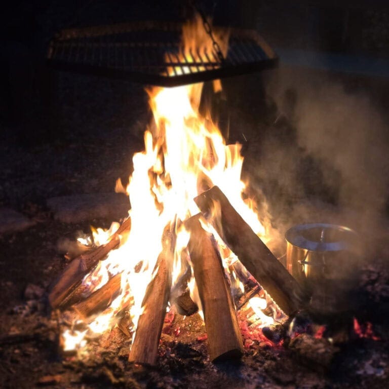 Feuerstelle mit brennendem Holz, Kochgeschirr und Flammen, ideal für Outdoor-Camping und Lagerfeuer.